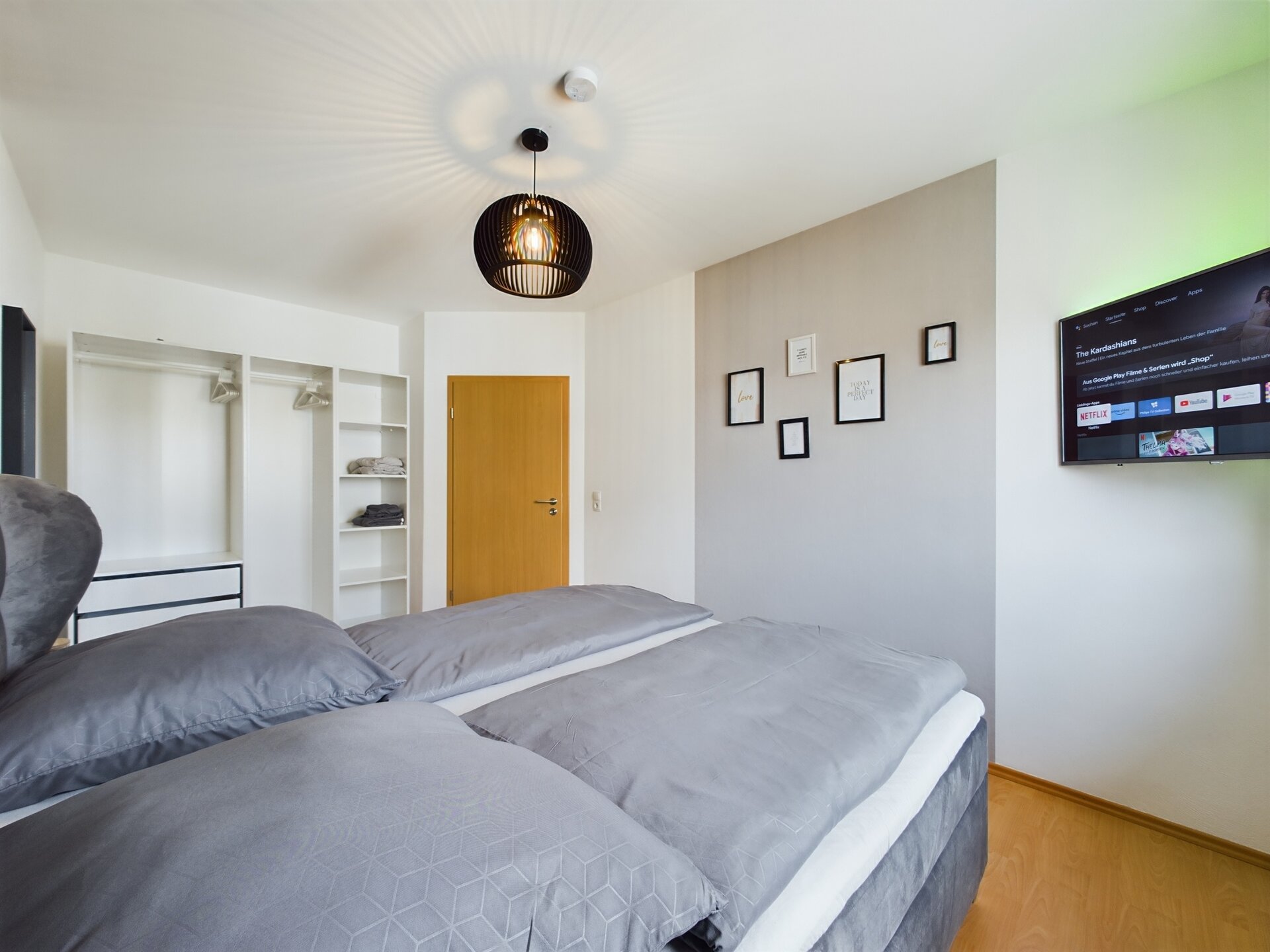 Modern bedroom with gray bedding and wall-mounted TV near Ramstein Air Base.