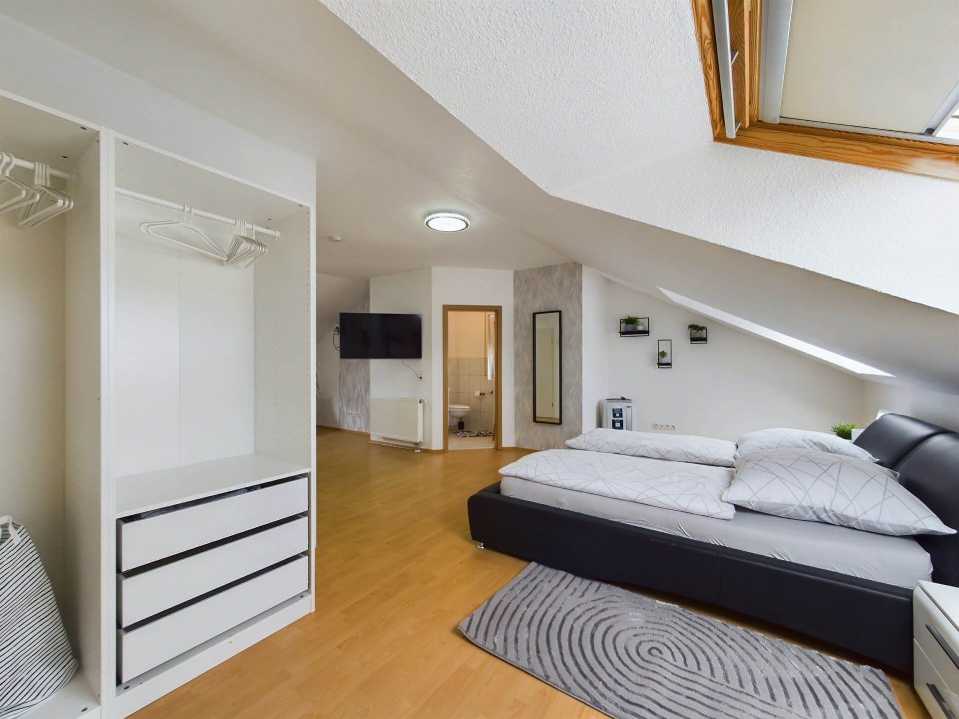 Modern bedroom with a sloped ceiling, large window, and minimalist decor in a spacious TLA house nea.